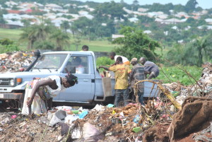 Imagem de uma viatura que vascula o lixo e as pessoas ao lado da viatura para aproveitar algo de bom que nele possam encontrar